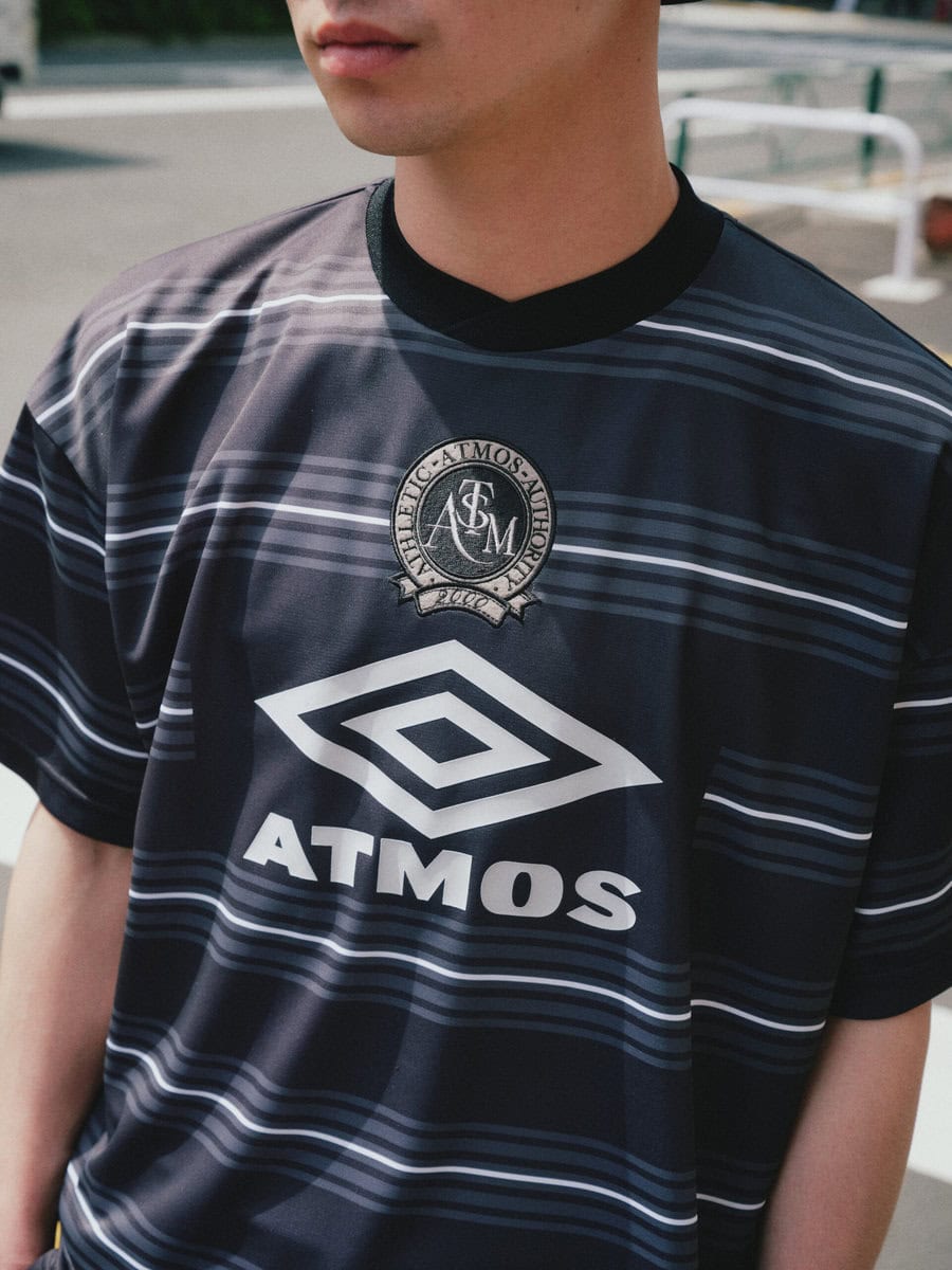 90年代の名門サッカークラブチームのユニフォームからインスピレーションを受けた半袖シャツは、フロントにUMBROとatmosのコラボロゴをプリント。オリジナルのボーダー柄とレトロな配色から、ヴィンテージライクな雰囲気が漂う。