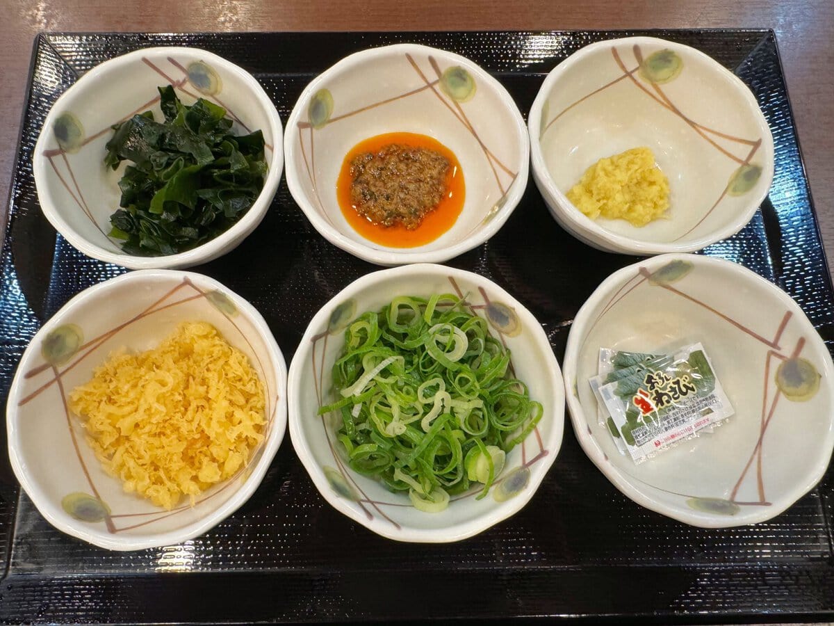 従来の6種類の薬味（青ねぎ、おろししょうが、天かす、香七味、すりごま、わさび）に加えて、新たにわかめとしび辛ラー油が追加され、全8種の展開になった無料の薬味＆トッピング