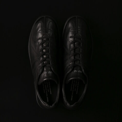 また、素材にはイタリア産のホースハイド(馬革)を採用。通常モデルのカウレザーよりも艶感と耐久性を兼ね備えた質感が特徴的。さらに、ロゴは鏡映しに配置され、既存のアイコンを再解釈。ソールは1970年代にスペインの老舗サプライヤーがテニス用に開発したカップソールを使用し、イタリアンホースハイドと直接縫い付ける「サイドマッケイ製法」で仕立てることで、唯一無二の佇まいを実現した。