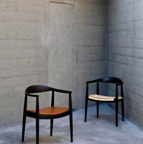 ウェグナー PP68 ザ・アームチェアのレザー座面と籐座面の2脚。深い色合いの木部とコンクリート壁の空間。