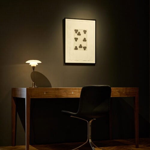 北欧ヴィンテージ風のデスクとワークスペース。鍵穴付きの木製ライティングデスク、ルイスポールセンのPHテーブルランプ、黒いレザーのデスクチェア。ミニマルな書斎のインテリア。