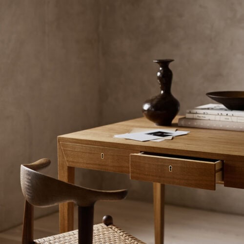 北欧モダンな木製デスクとハンス・J・ウェグナー風のチェア。真鍮の鍵穴があるオーク材のデスク、ペーパーコード座面の椅子。陶器の花瓶と本が置かれたナチュラルなインテリア。