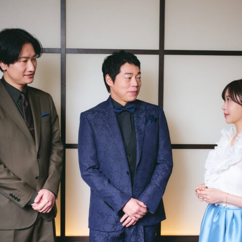 エレガントなビジネススーツを着た男性二人と、白いドレスの女性が会話を楽しむシーン.