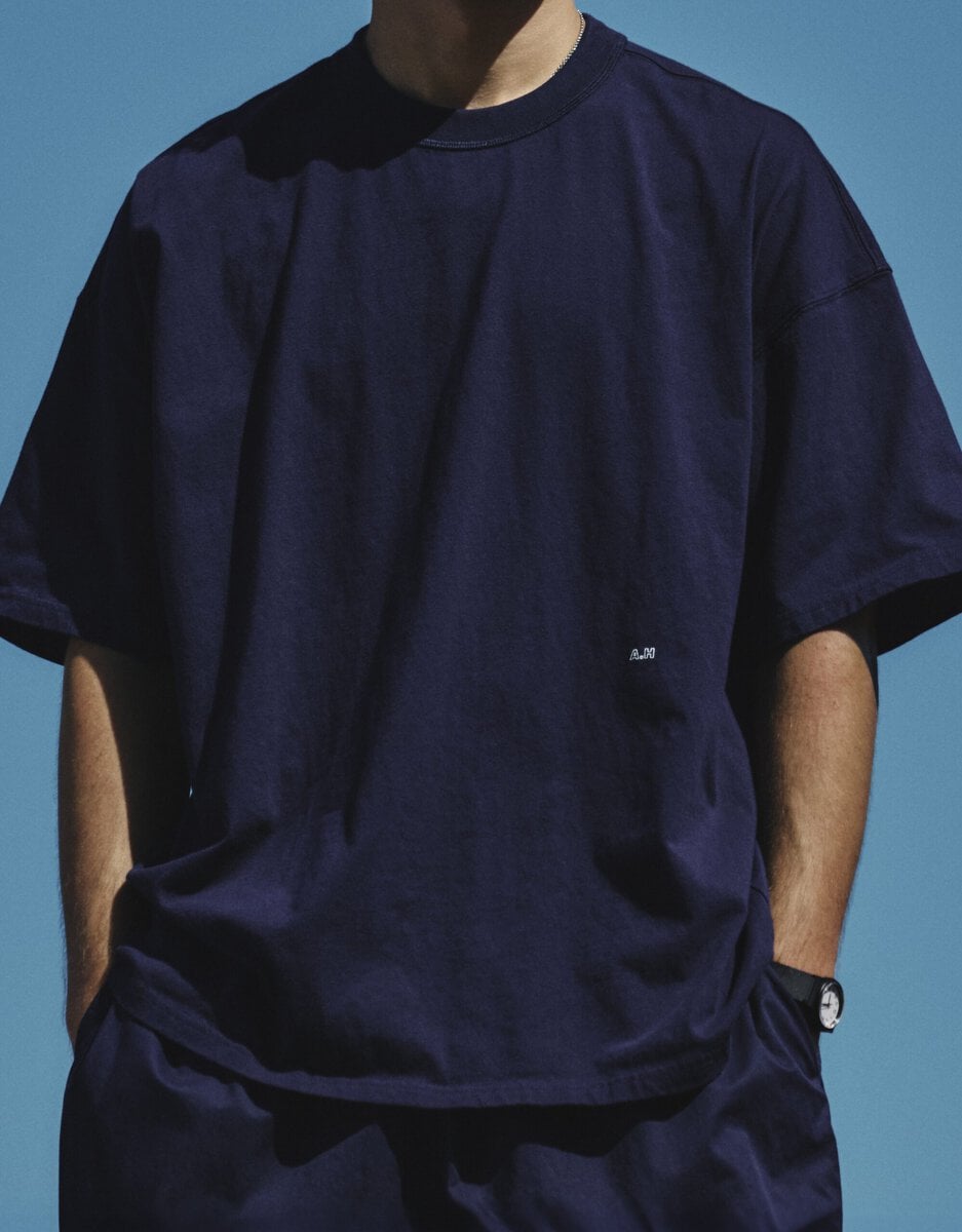 コンビニエンスウェアを代表する無地のアウターTシャツを、「A.H」らしいビッグシルエットで表現した男女兼用モデル。前身頃には「A.H」のロゴを小さく配置。しろとネイビーの2色を用意し、XXL相当のワンサイズで展開している。