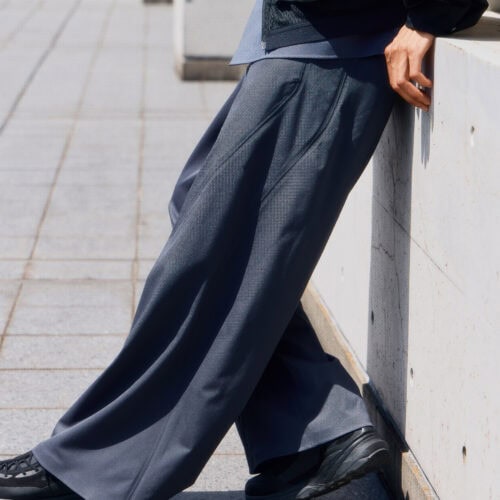 ノータックのすっきりとした腰まわりから、裾までまっすぐに落ちるワイドストレートパンツ。身体のラインを拾いにくい適度なゆとりと、ウールのしなやかなドレープが端正なフォルムをつくっている。
