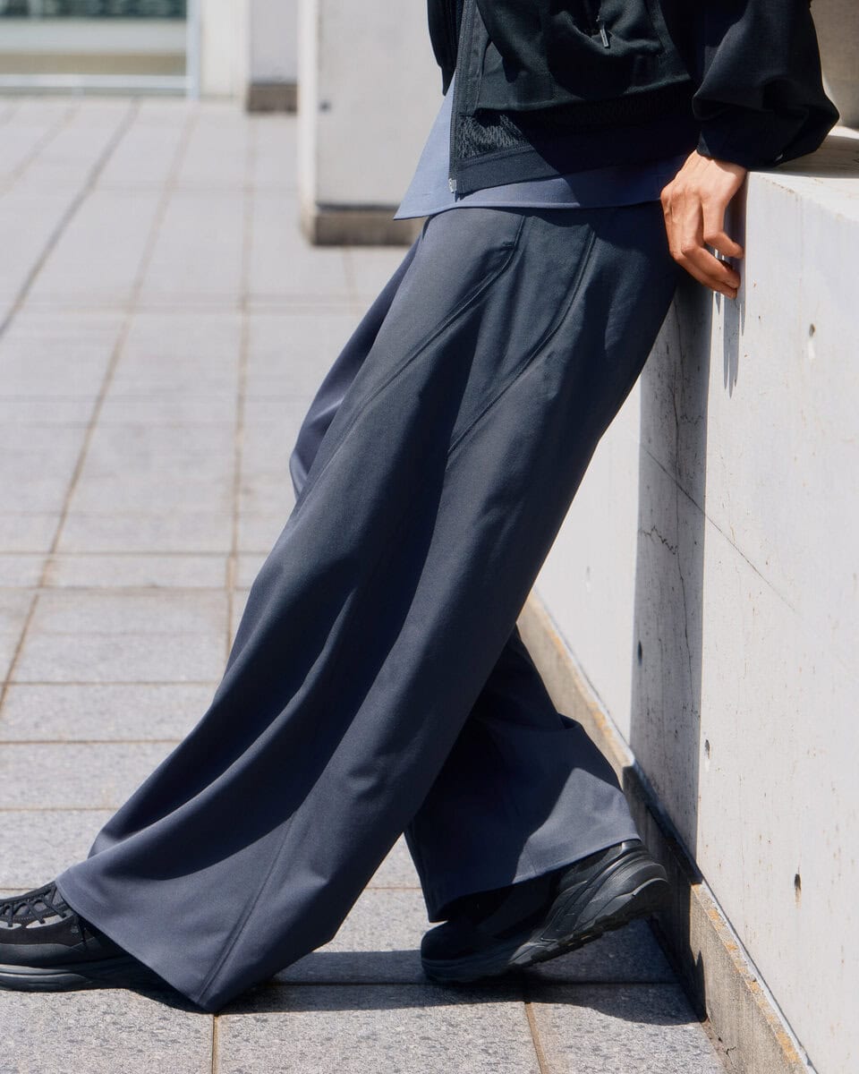 ノータックのすっきりとした腰まわりから、裾までまっすぐに落ちるワイドストレートパンツ。身体のラインを拾いにくい適度なゆとりと、ウールのしなやかなドレープが端正なフォルムをつくっている。